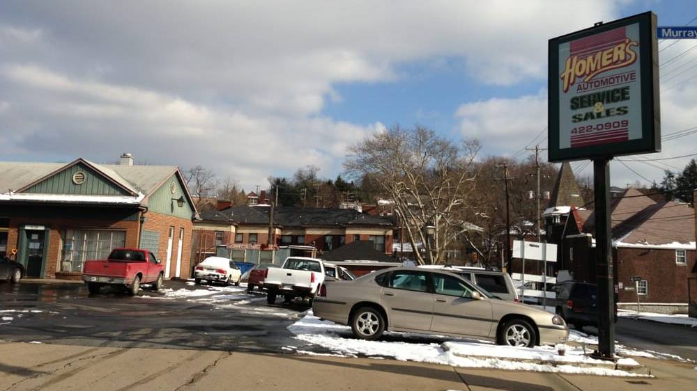 The Homer&rsquo;s Automotive Service & Sales sign on Murray Avenue beside the brick and green garage, with cars parked on a snowy lot.
