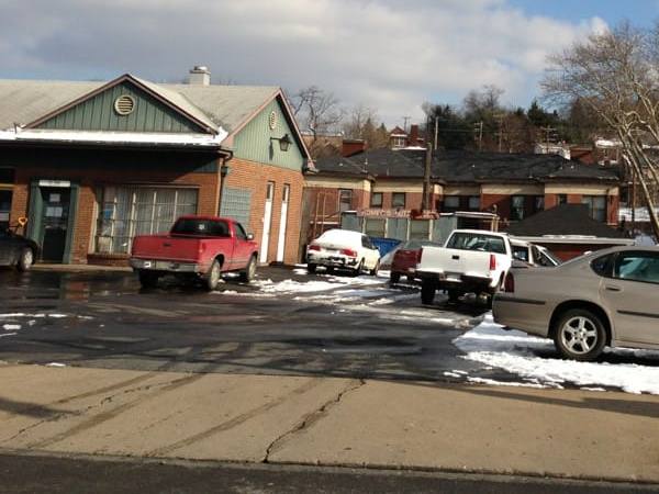 The brick and green-trimmed Homer&rsquo;s garage on Murray Avenue, with a red pickup, a white truck and a tan sedan parked in a snowy lot.